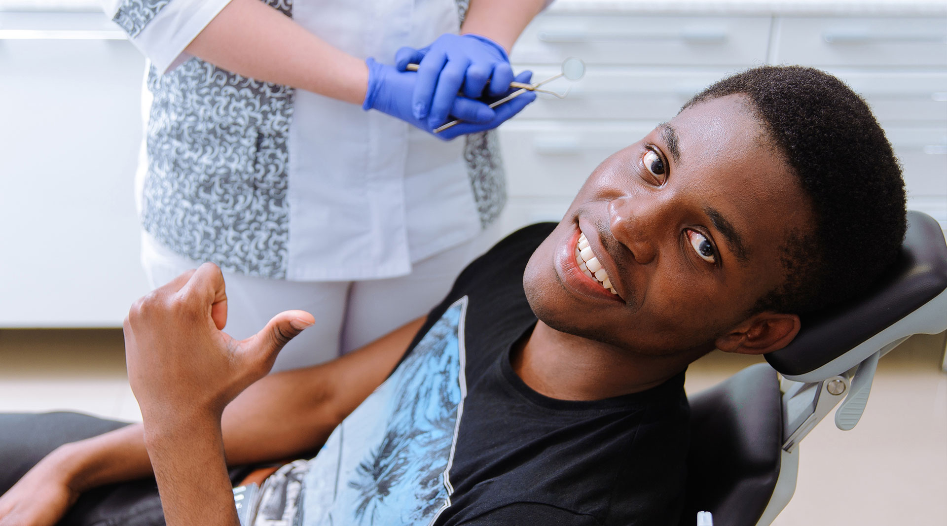 A young man receiving dental care, smiling at the camera, with a dental hygienist administering treatment.