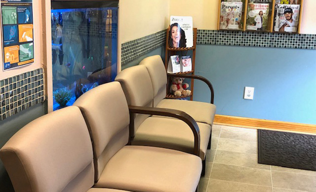 The image shows an interior space with a seating area featuring beige chairs and a blue wall, along with a sign and a fish tank in the background.