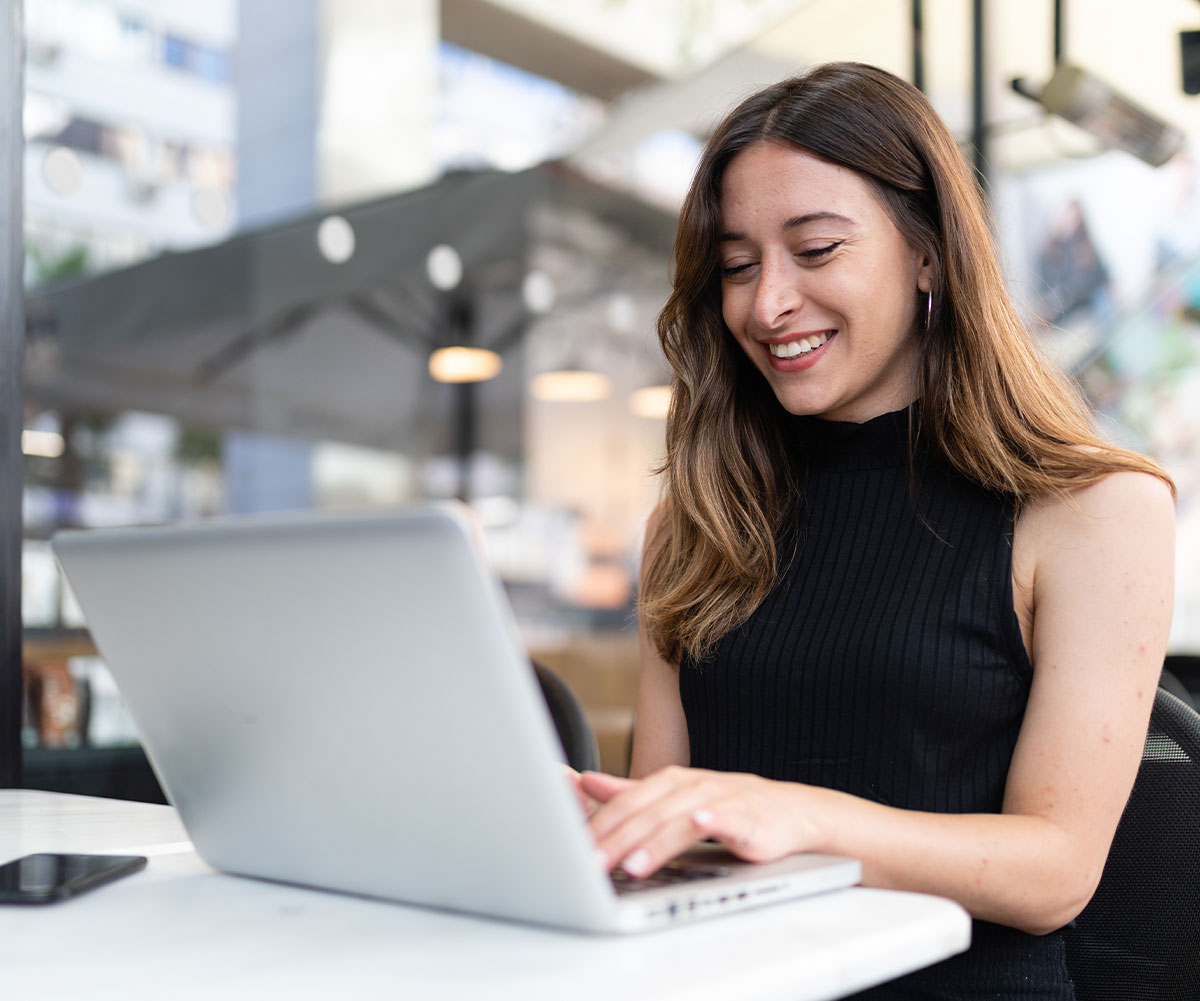 A smiling woman in a black top using a laptop on a table.