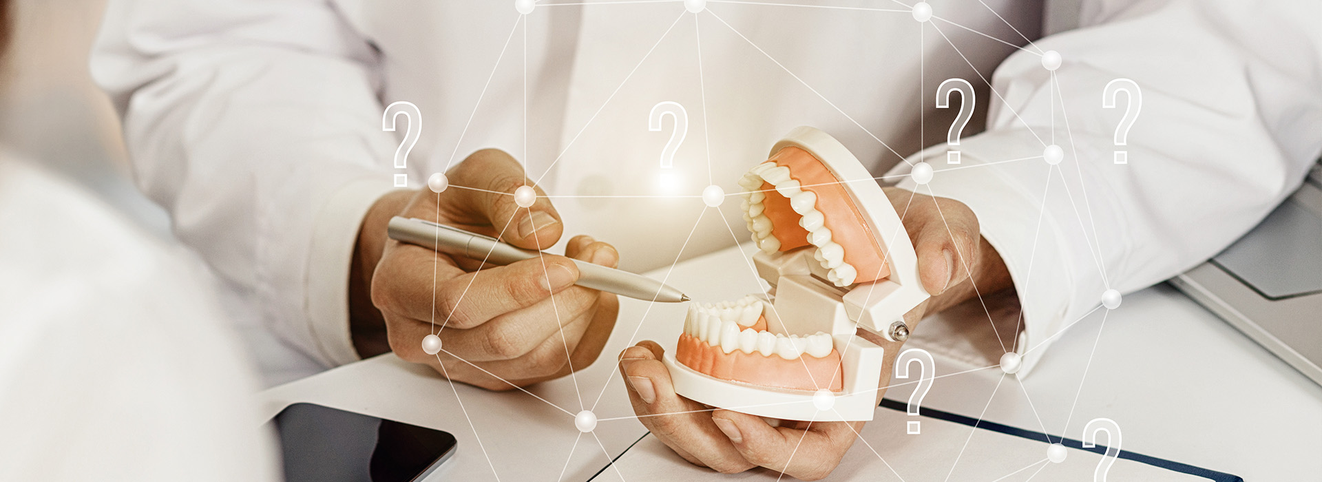 The image shows a person holding a model of a human mouth with teeth, while another individual appears to be examining a digital display related to dental health on a tablet.