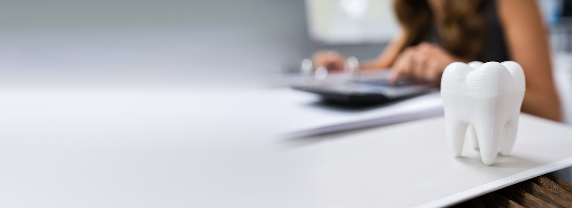 A person sitting at a desk with a laptop, papers, and a toothbrush-shaped object on a table in front of them.