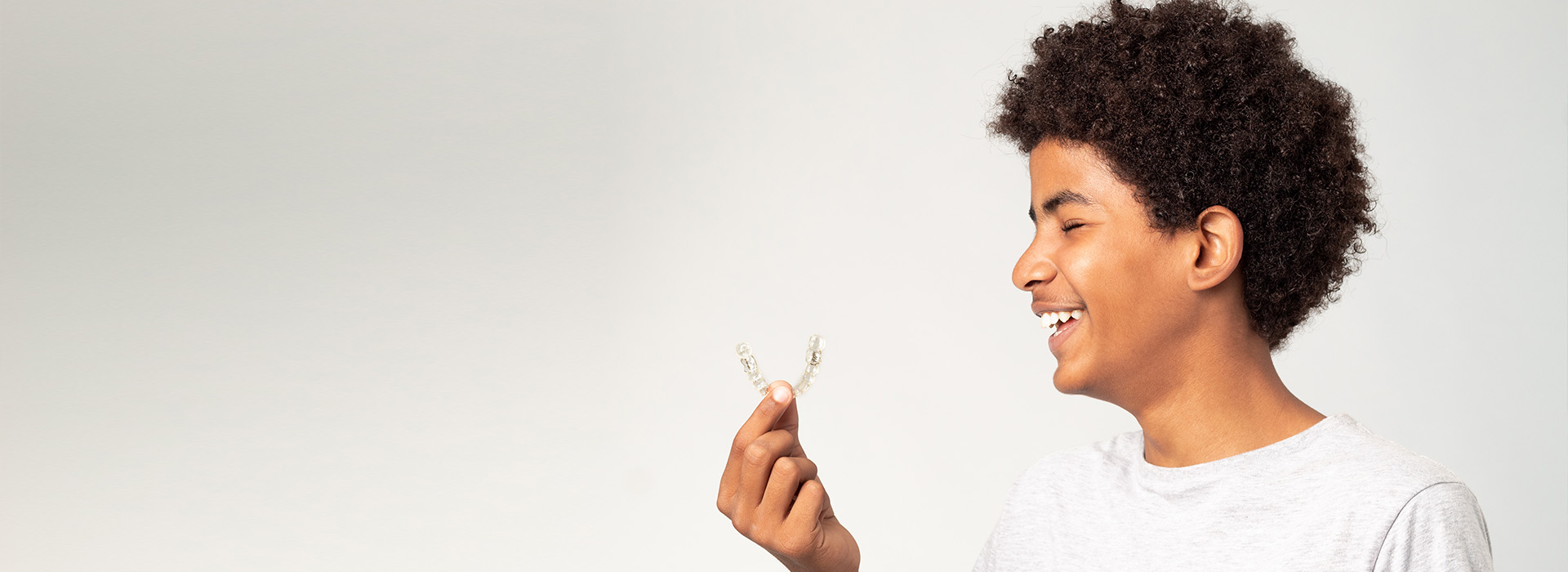 A young person holding a flower with a joyful expression, set against a plain background.