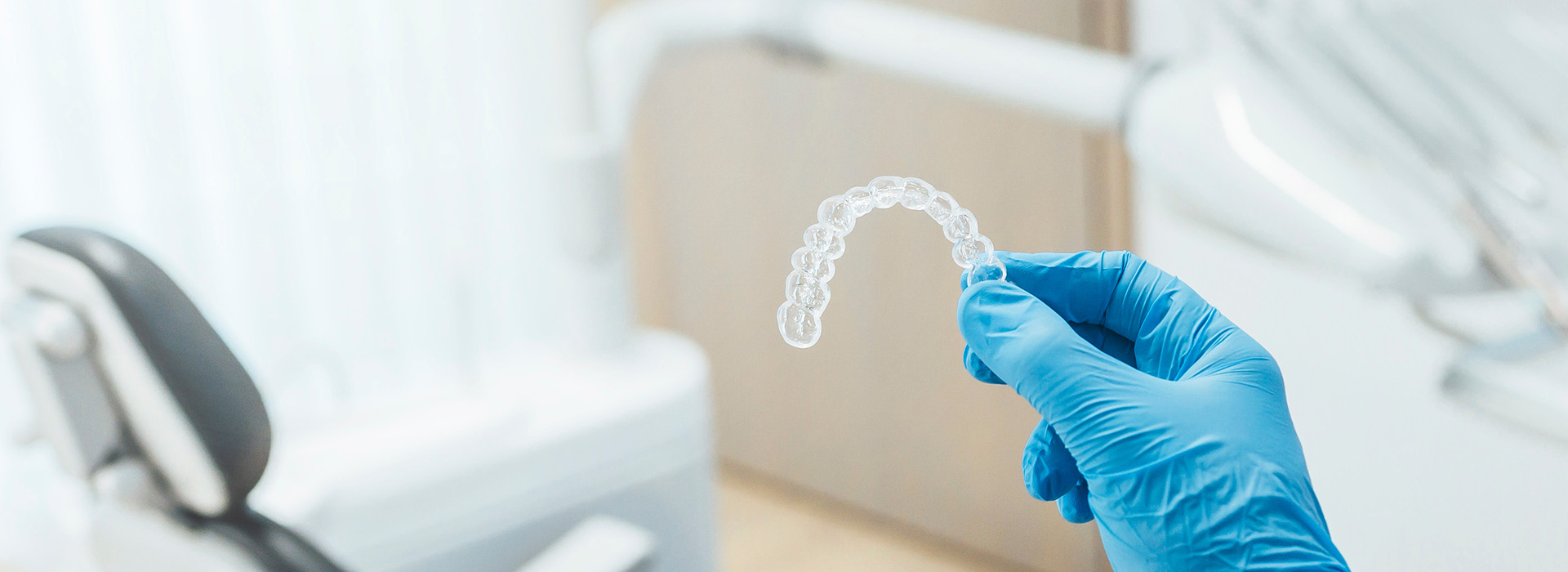 An individual s hand holding a transparent dental implant over a dental chair, with a focus on dental care equipment in the background.