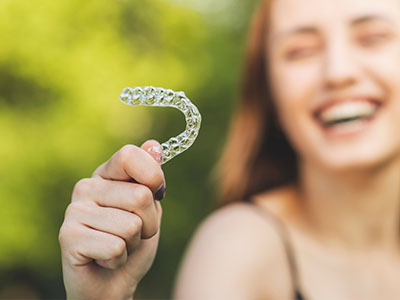 A smiling woman holding a clear plastic mouthguard with her left hand.