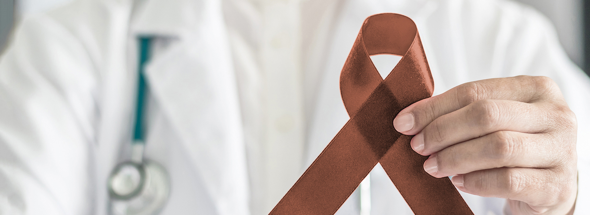 The image features a healthcare professional holding a brown ribbon with a red symbol, likely representing awareness for a specific medical condition or cause, set against a clinical background.