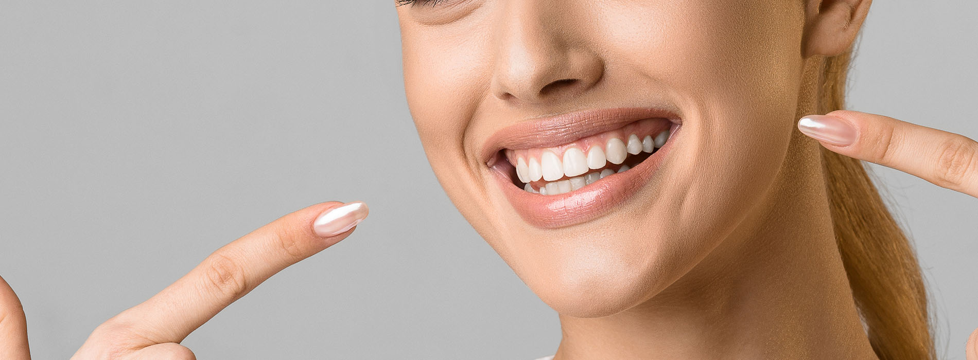 A woman with a radiant smile holds up two fingers on each hand, showcasing her clean, manicured nails against a neutral background.