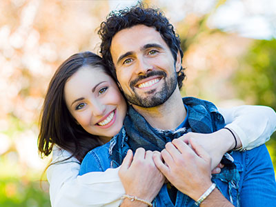 A man and woman are embracing each other in a joyful pose against a blurred background.