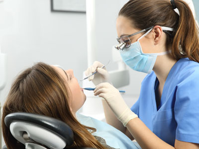 A dental hygienist wearing gloves and a mask is attending to a patient receiving dental care.