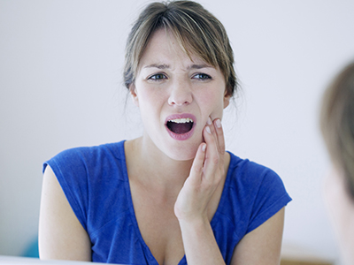 The image depicts a woman with her mouth open, showing teeth, while holding her hand up to her face. She appears to be expressing surprise or shock.