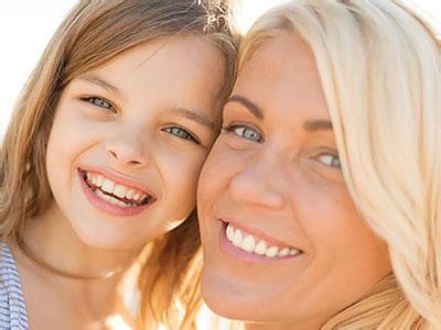 The image shows a woman and a child smiling at each other against a blurred background.