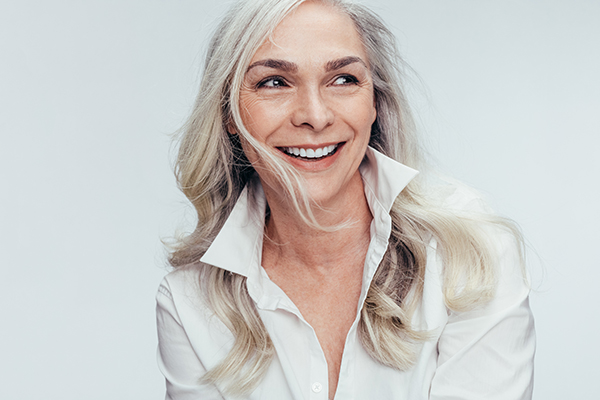 A smiling woman with gray hair, wearing a white shirt and sunglasses, posing for a portrait.