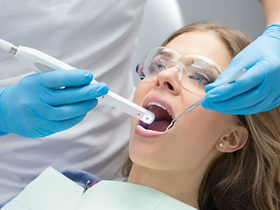 A woman receiving dental care with a dental device inserted into her mouth by a dental professional wearing blue gloves and a surgical mask.