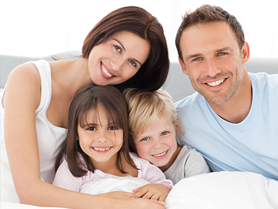 A family of four posing together on a bed with smiles.