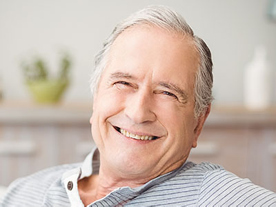 The image shows an older man with gray hair smiling broadly while sitting in a relaxed pose.